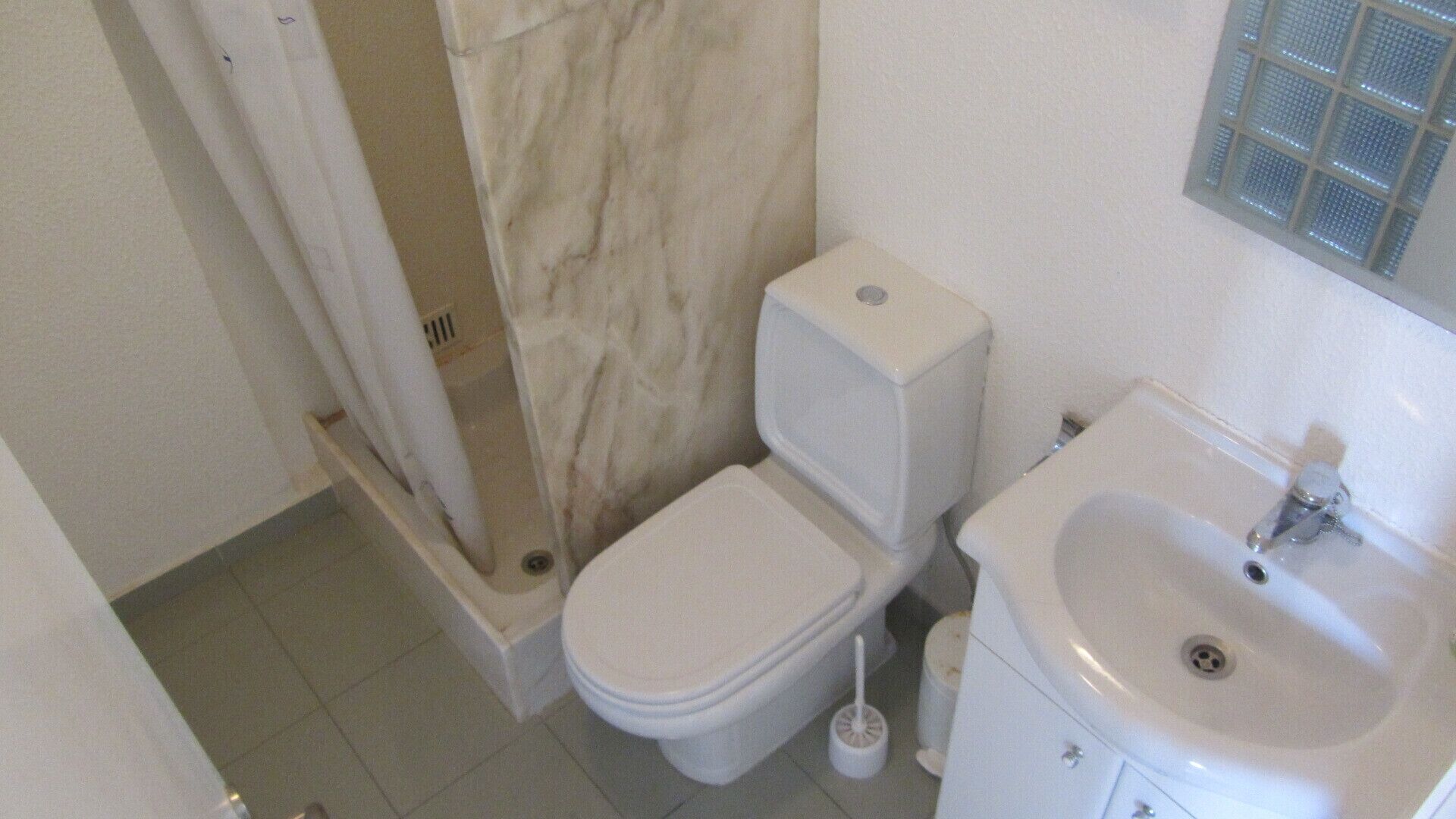 Une petite salle de bain blanche, équipée de toilettes, d’un lavabo et d’une douche.