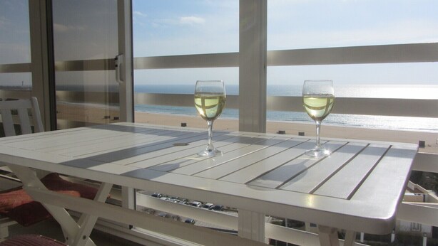Una mesa con dos copas de vino blanco, con vista a una playa.