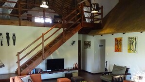 Un vaste espace de vie doté d’un haut plafond, d’un escalier en bois, d’un grand canapé, d’une table basse et d’œuvres d’art accrochées aux murs.