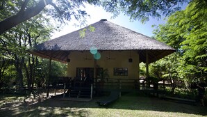 Un pavillon à toit de chaume, doté d’un escalier menant à une porte, et entouré d’arbres.