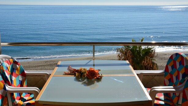 A table with a vase of flowers, two chairs with colorful patterns, and a view of the ocean and beach. - Roca Bajondillo magnificent sea views, two bedrooms, parking, free wifi (Torremolinos)