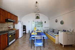 A kitchen with a dining table, chairs, and a built-in oven. There is a white refrigerator, wooden cabinets, and a hanging light fixture.
