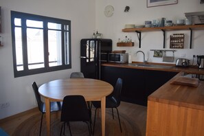 A compact kitchen with a dining table, chairs, a refrigerator, microwave, and a coffee maker.