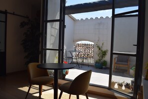 A room with two chairs and a table, large windows, and potted plants.