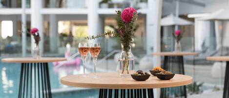 Ein Tisch am Pool mit zwei Gläsern Roséwein, einer Vase mit einer rosa Blume und einer Oliven-Schale.