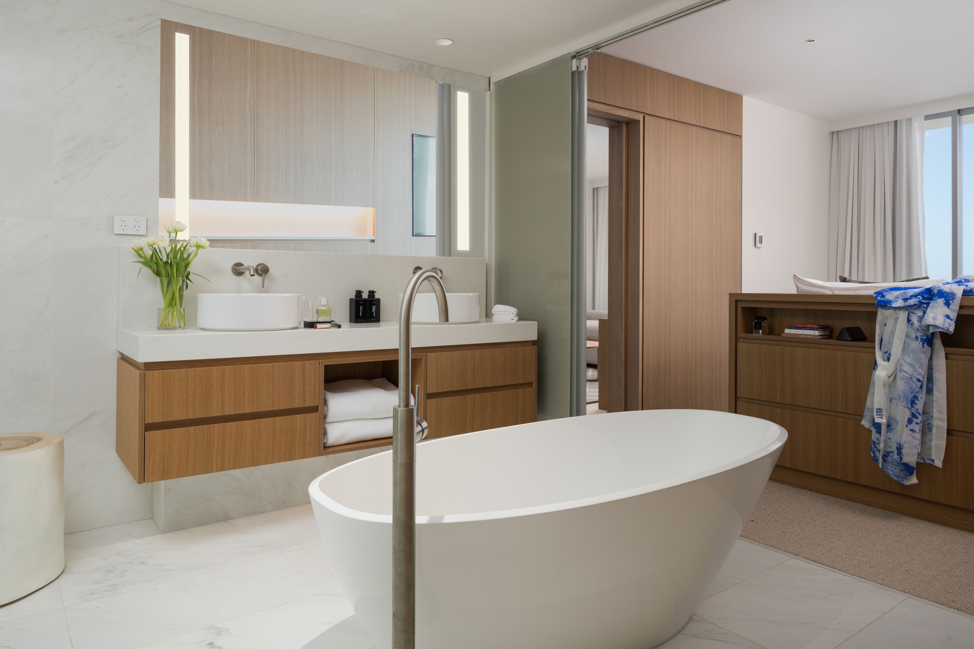 Un baño moderno con una bañera independiente, armarios de madera, un espejo grande y un perchero para toallas.