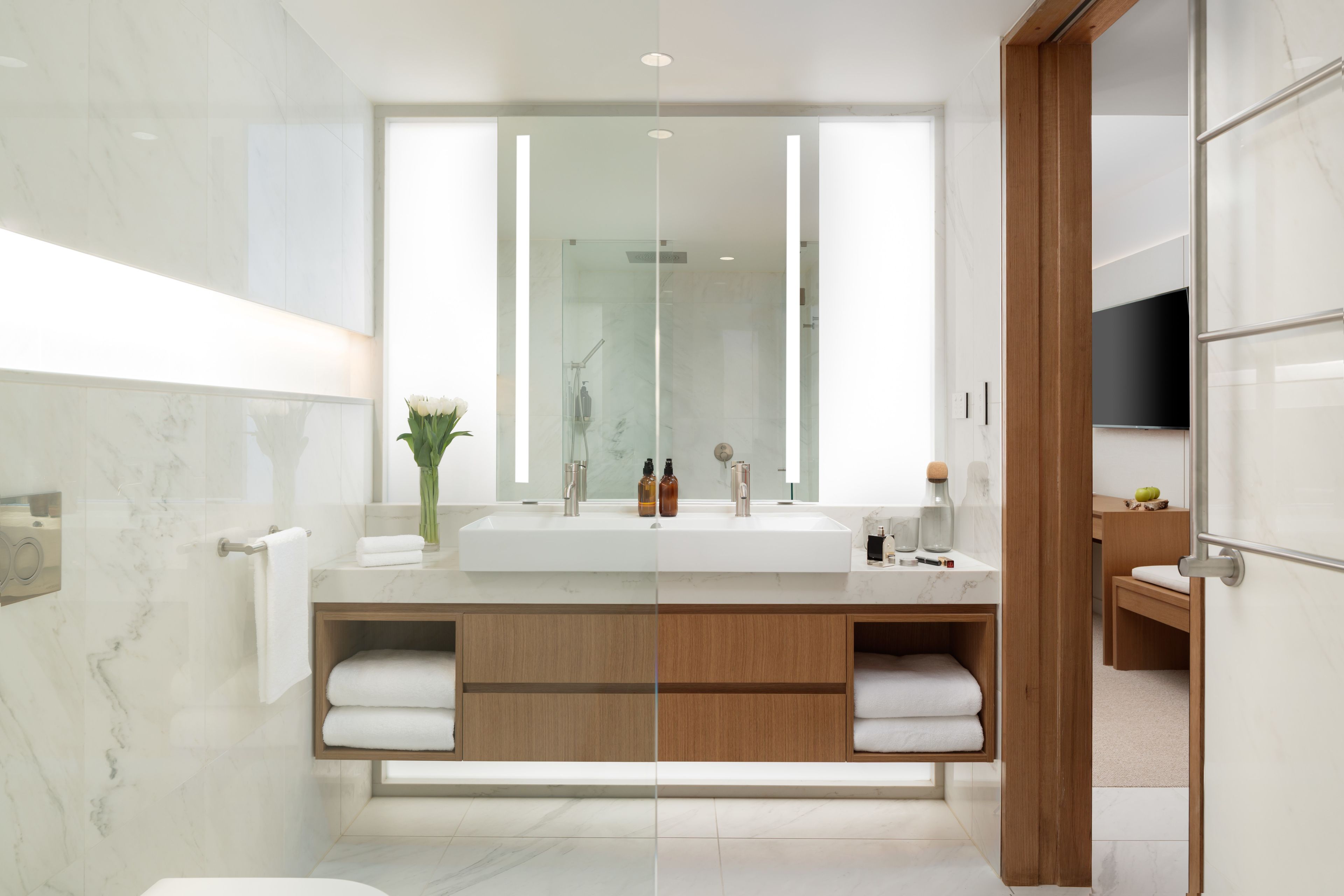 A modern bathroom with a large mirror, dual sinks, wooden cabinetry, and a glass shower enclosure.