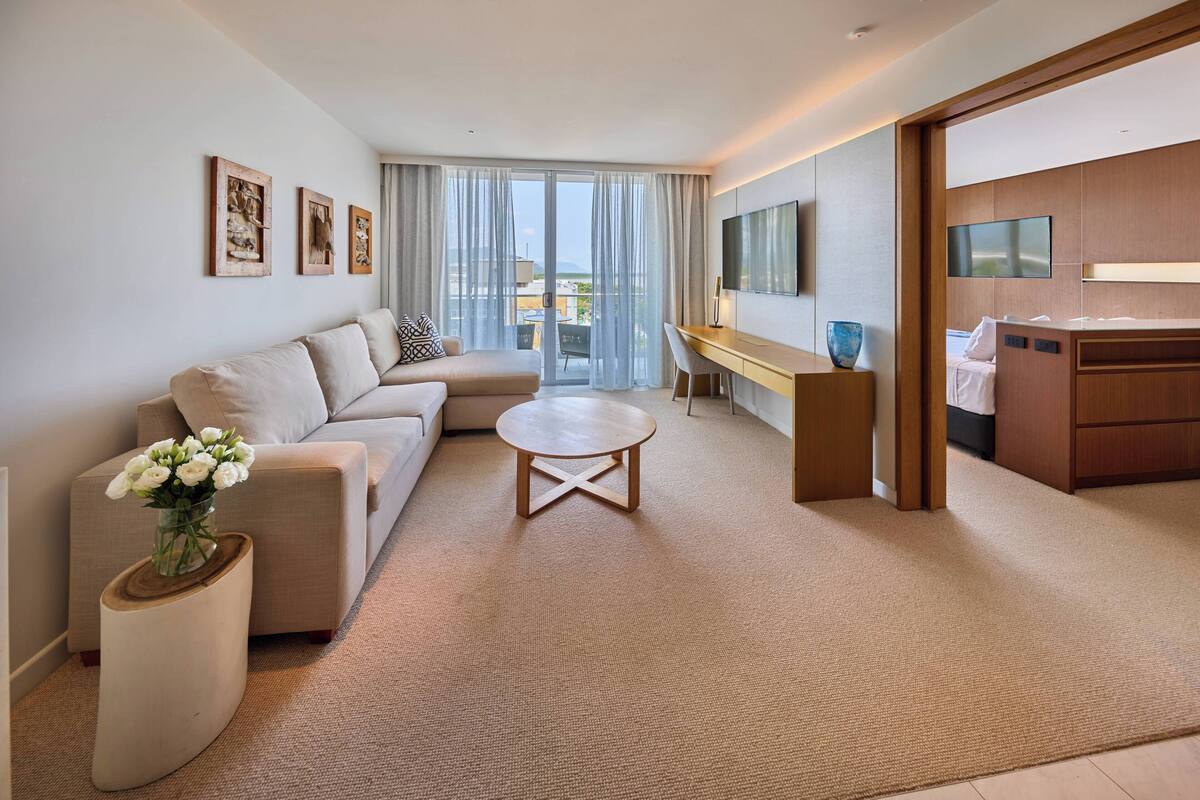 A modern hotel room with a sofa, a round coffee table, a desk, and a bed.