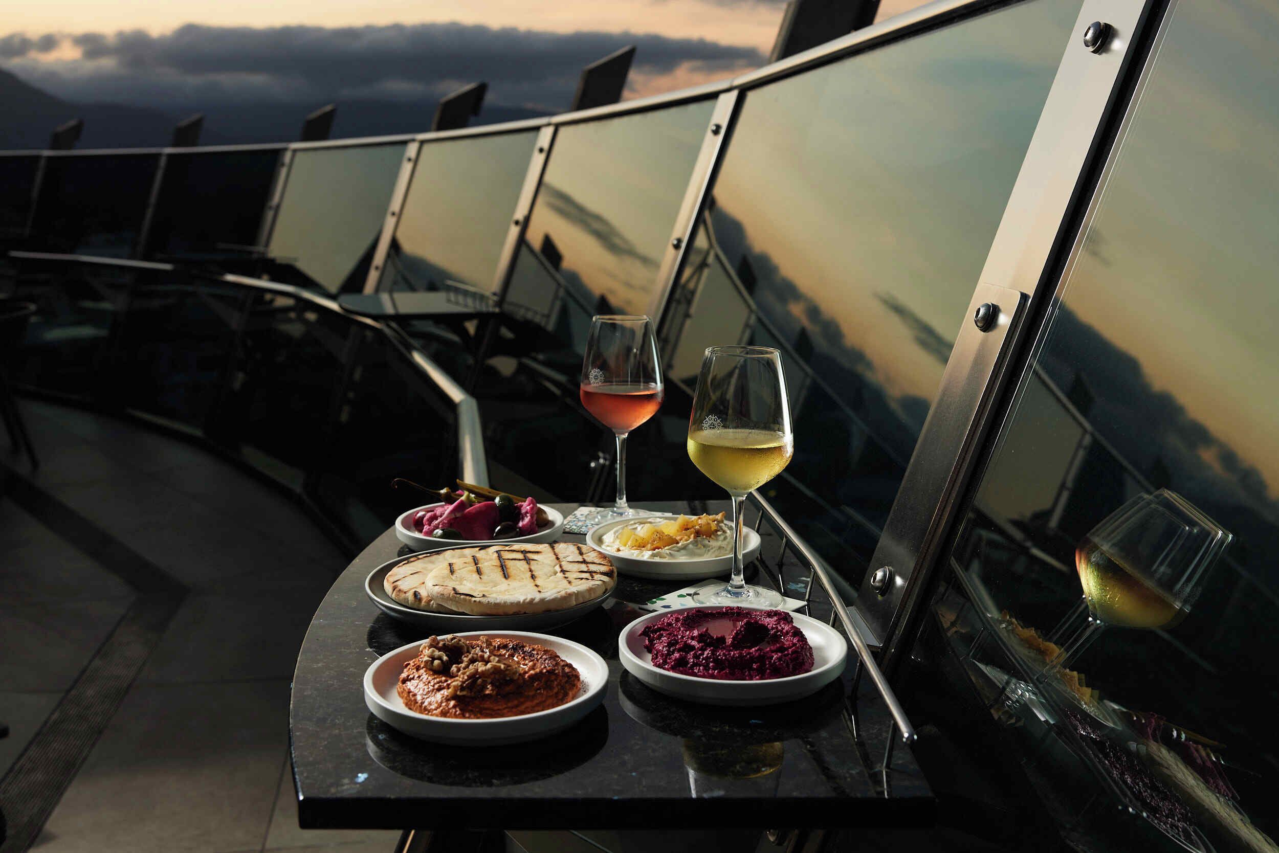 Una mesa con diversos platos y copas de vino, con vistas panorámicas al fondo.