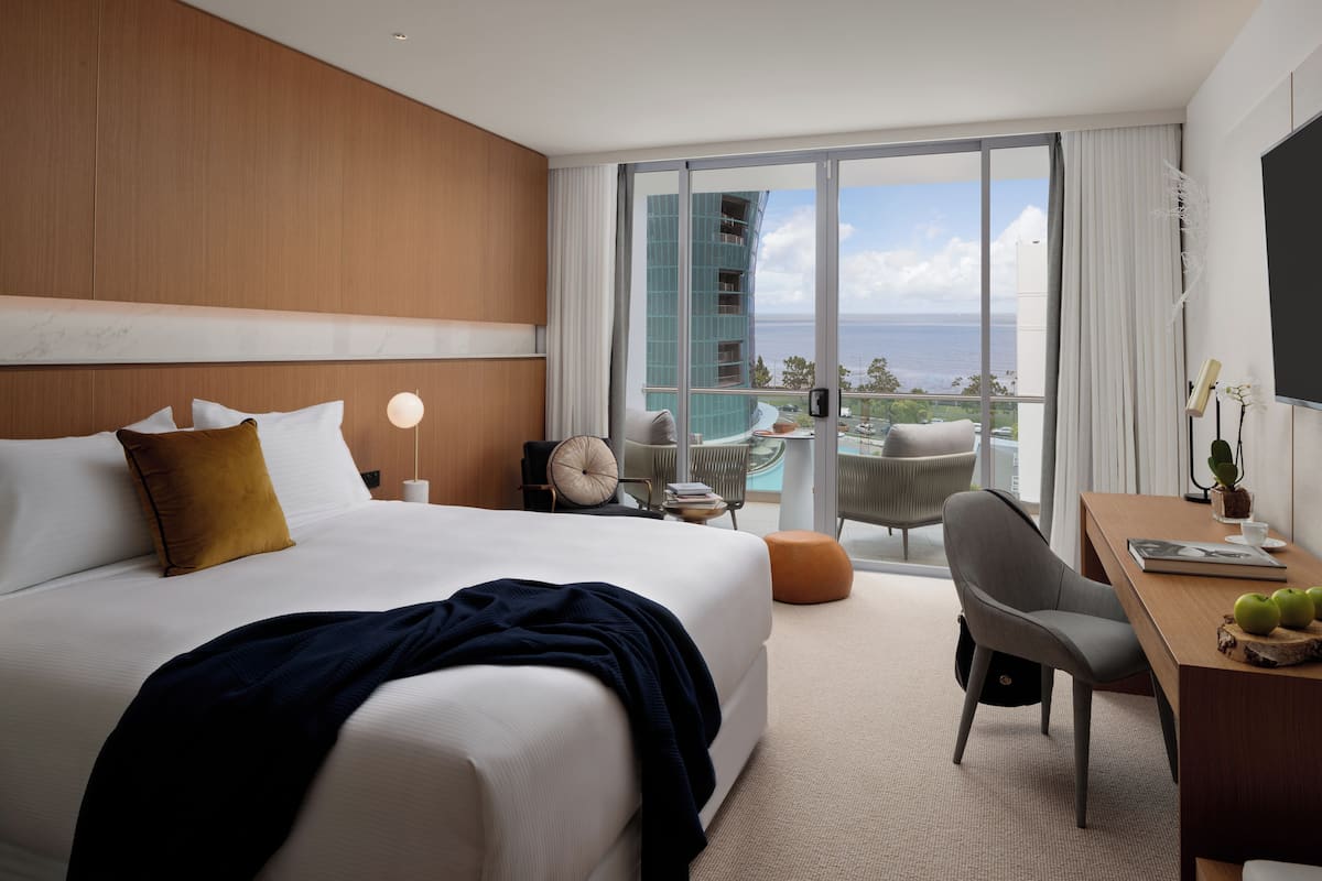 A modern hotel room with a large bed, a desk, and a view of the ocean.
