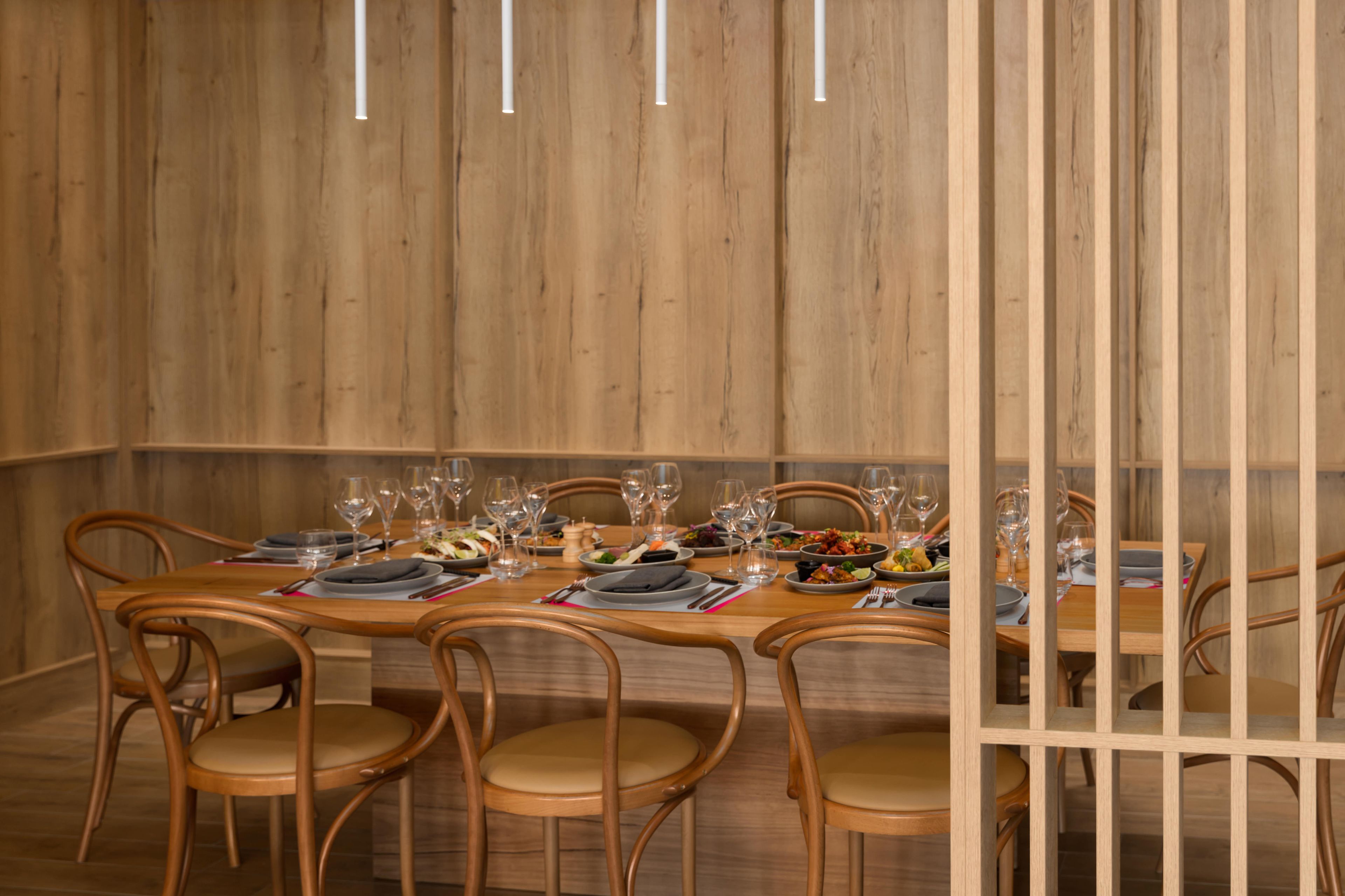 A dining area with wooden walls, a long table set for a meal, and several chairs.