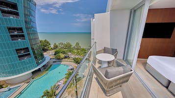 A balcony with a view of a swimming pool and ocean, a white sofa, and a dining table.