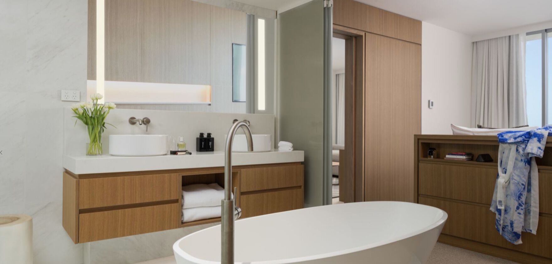 A modern bathroom with a freestanding bathtub, wooden cabinetry, a vanity with a mirror, and a towel rack.