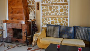 A cozy living room with a brick fireplace, a yellow sofa, patterned cushions, and a stone wall. - Beach house with medieval charm in Chilches Costa (Velez-Malaga)