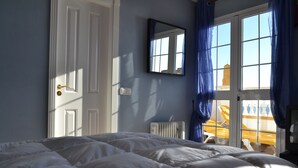 A bedroom with a bed, a window with curtains, a radiator, and a door. - Beach house with medieval charm in Chilches Costa (Velez-Malaga)