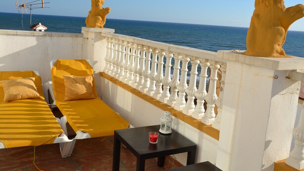 A balcony with a white balustrade, two lion statues, a yellow sofa, a small table with a candle, and a view of the sea. - Beach house with medieval charm in Chilches Costa (Velez-Malaga)