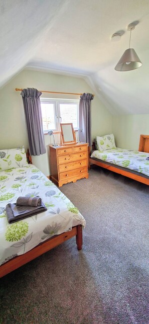 A bedroom with two single beds, a wooden dresser, and a ceiling fan.