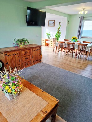 Un comedor con una mesa de madera, sillas, un televisor montado en la pared y una planta en maceta.