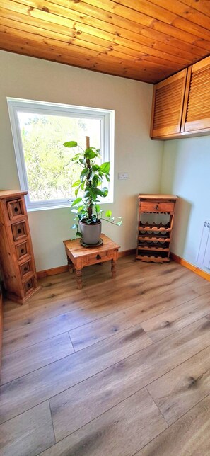 A room with wooden flooring, a window with a view of greenery, a wooden cabinet, and a small wooden table with a potted plant.
