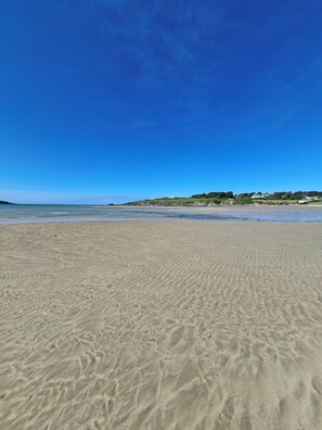 A sandy beach with a clear blue sky and a distant view of houses on a hill.