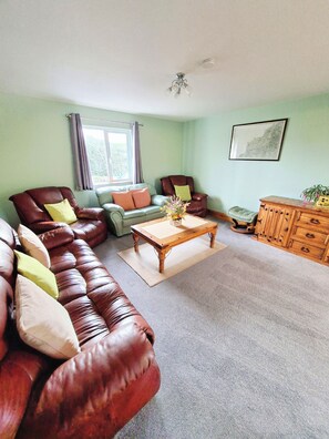 A living room with a brown leather sofa, a green armchair, a wooden coffee table, and a wooden cabinet.