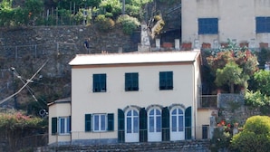 Ein zweistöckiges Gebäude mit rustiziertem Sockel und weißem Oberteil, mit einem Balkon und Blumentöpfen.