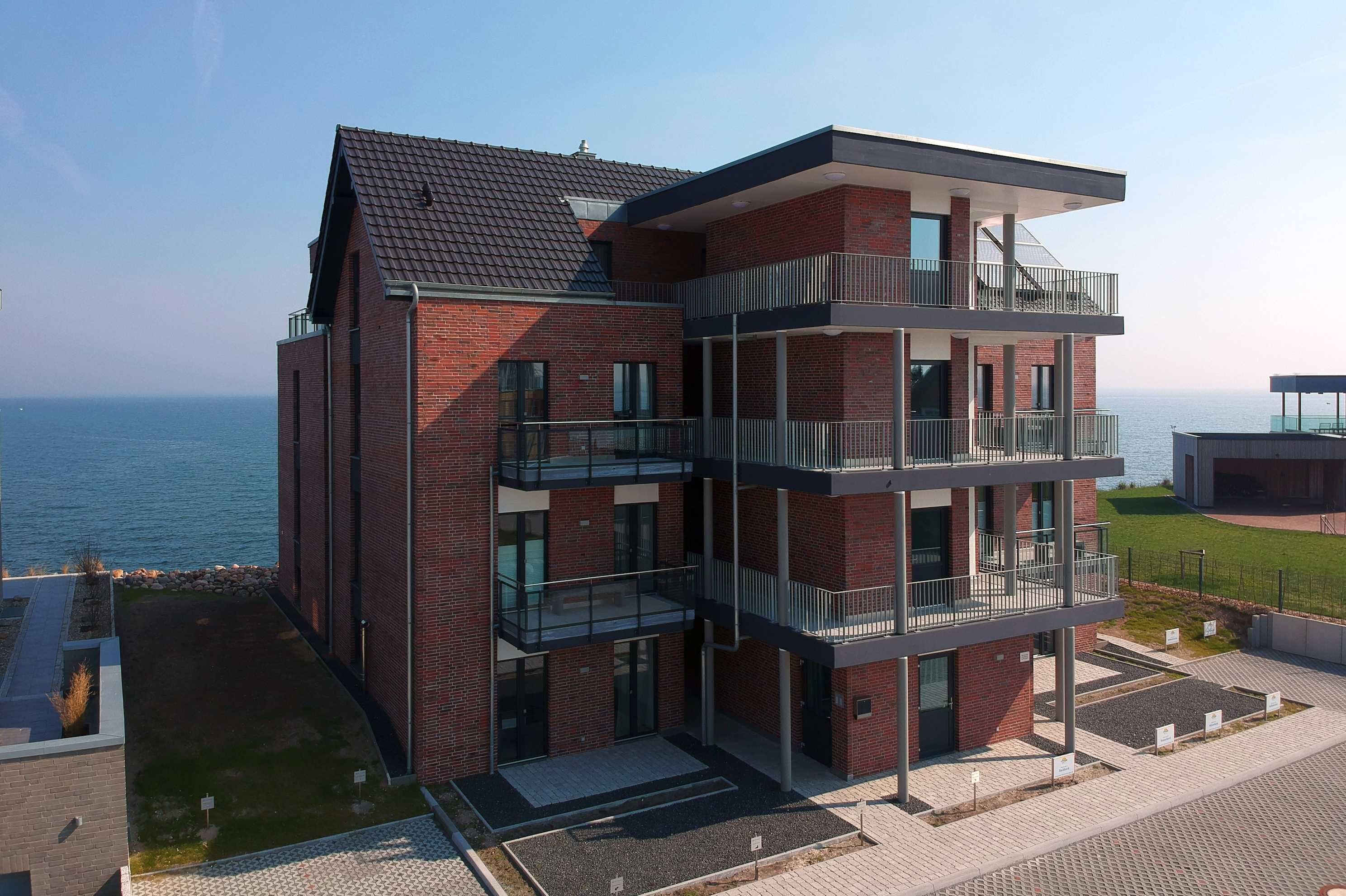 Un immeuble moderne à plusieurs étages, doté d’une façade en briques, de balcons et offrant une vue sur la mer.