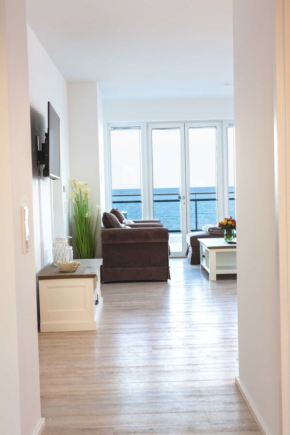 A modern living room with a large window, a sofa, a coffee table, and a TV mounted on the wall.