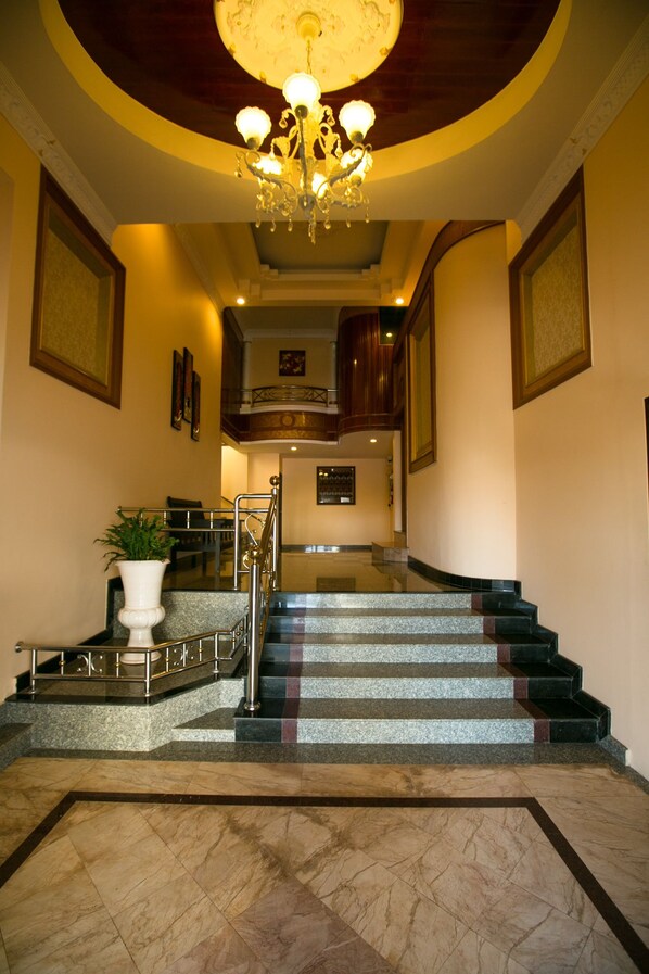 A grand staircase with a chandelier, marble steps, and a potted plant.