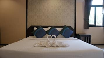 Una cama bien hecha con un arreglo de almohadas en forma de cisne, un cabecero estampado y una ventana con cortinas.