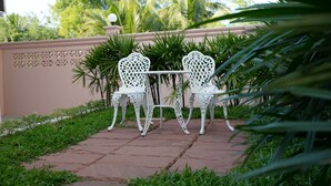 Une terrasse de jardin avec deux chaises blanches et une table, entourée d’une végétation luxuriante et d’un mur rose.