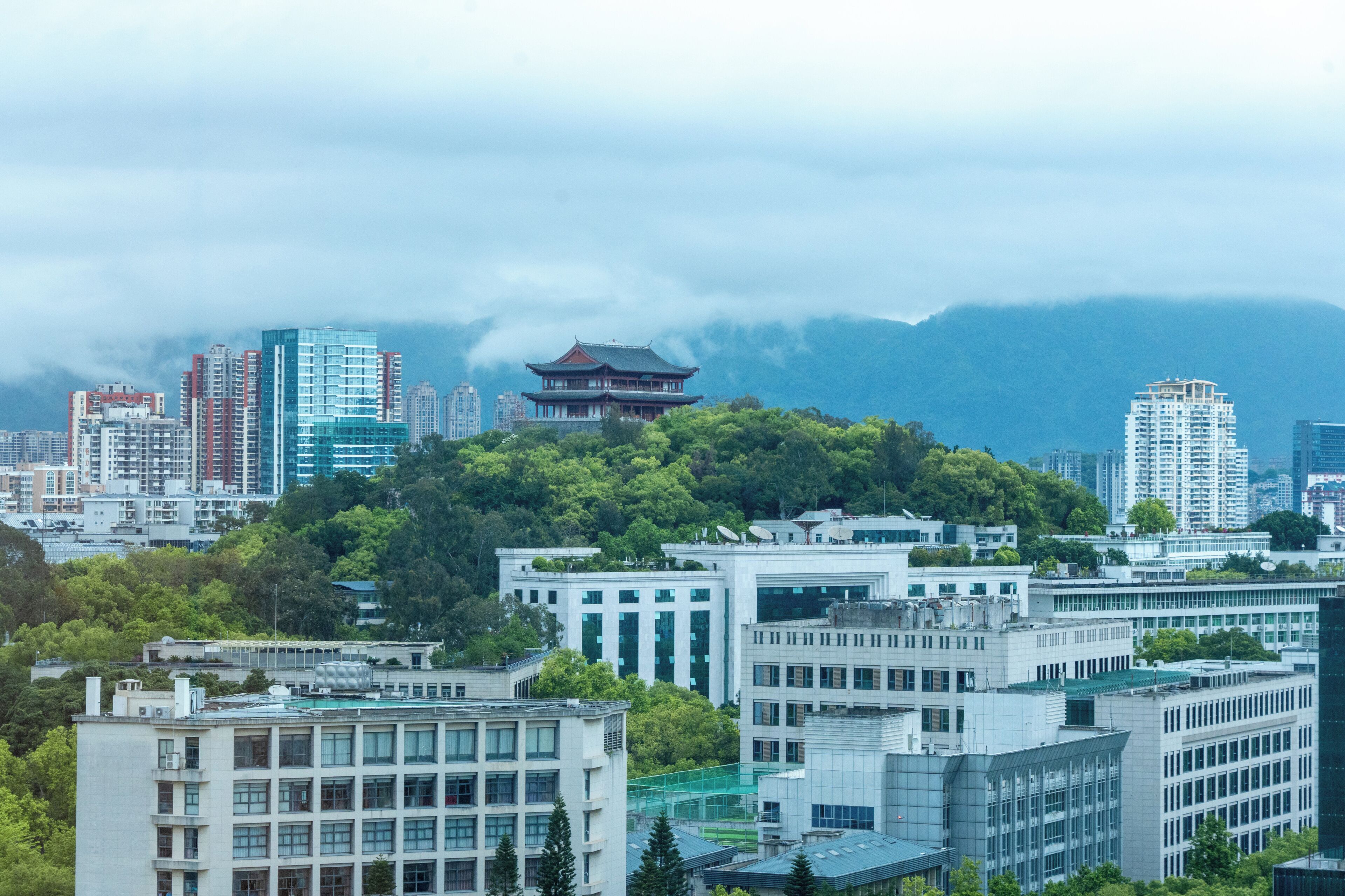 A cityscape with modern buildings, a traditional pagoda, and a mountain backdrop.