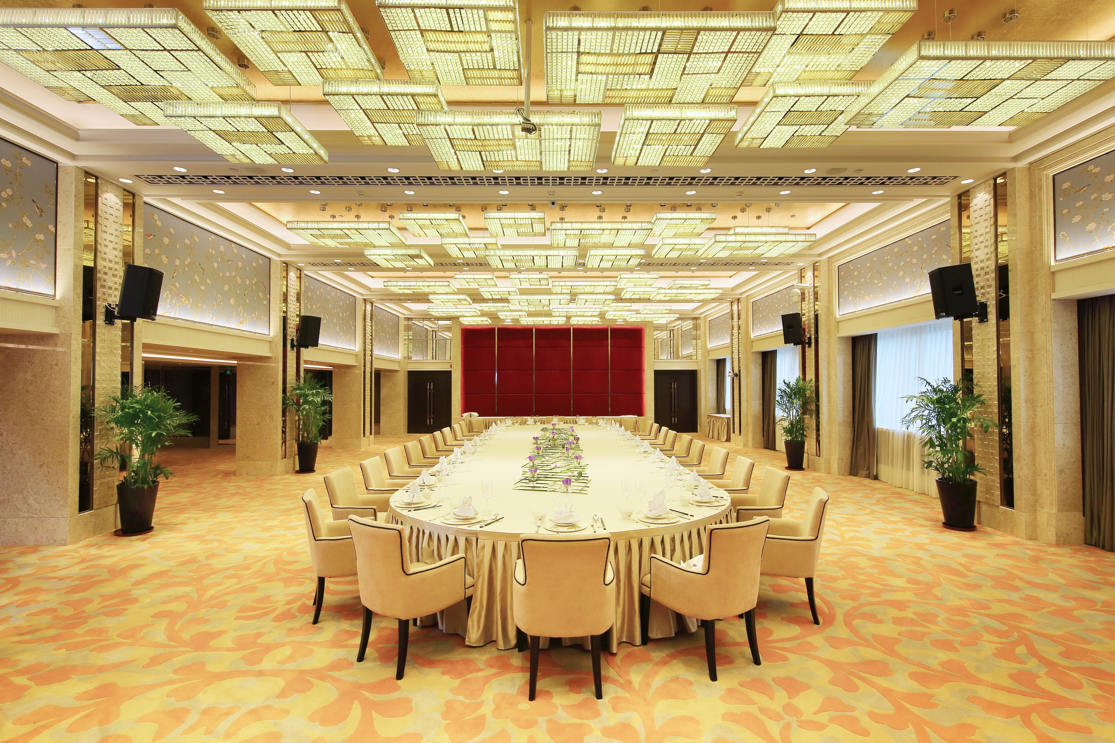 Une grande salle de conférence avec une longue table, des chaises de couleur beige et un tapis à motifs.