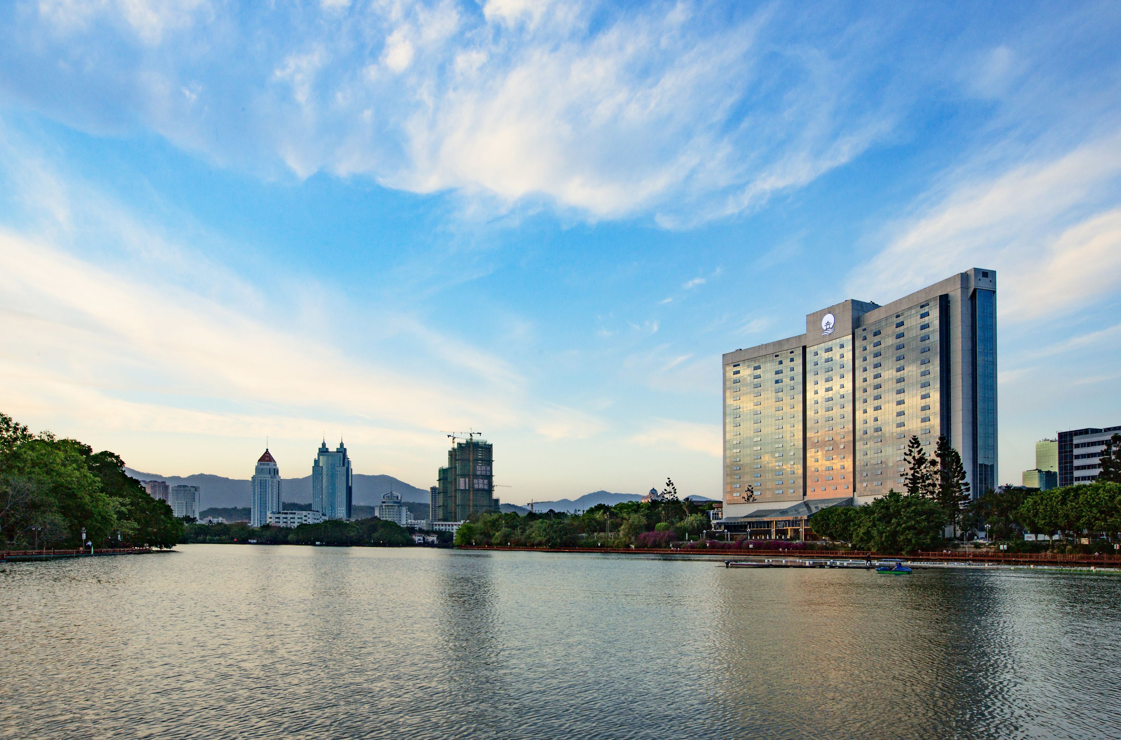 A high-rise hotel with a modern design, situated by a body of water with a clear sky.