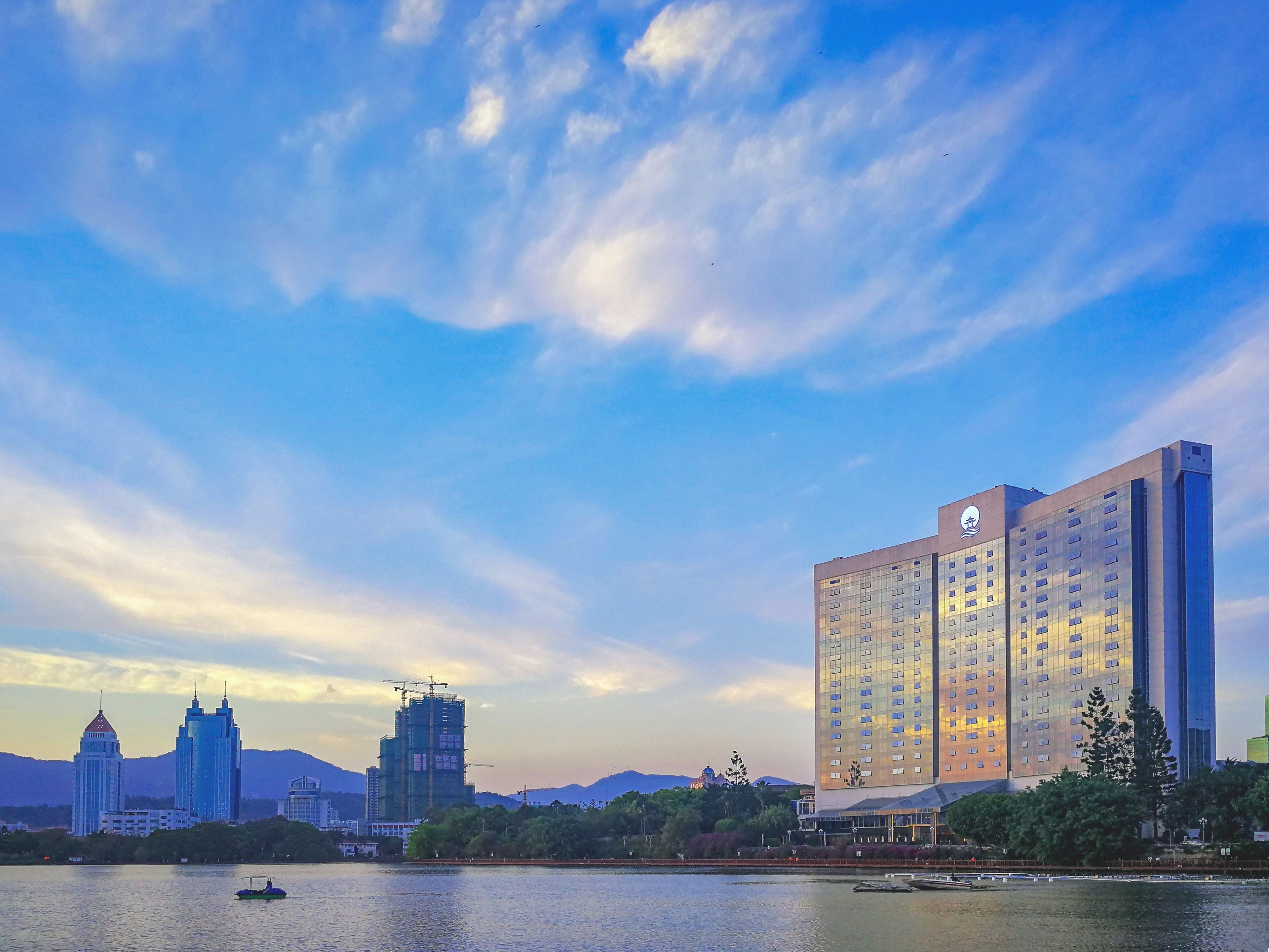 A high-rise hotel with a modern design, located near a body of water with a boat visible.