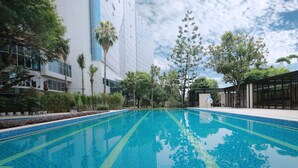 Una piscina con azulejos azules, rodeada de árboles y un edificio moderno con grandes ventanales.