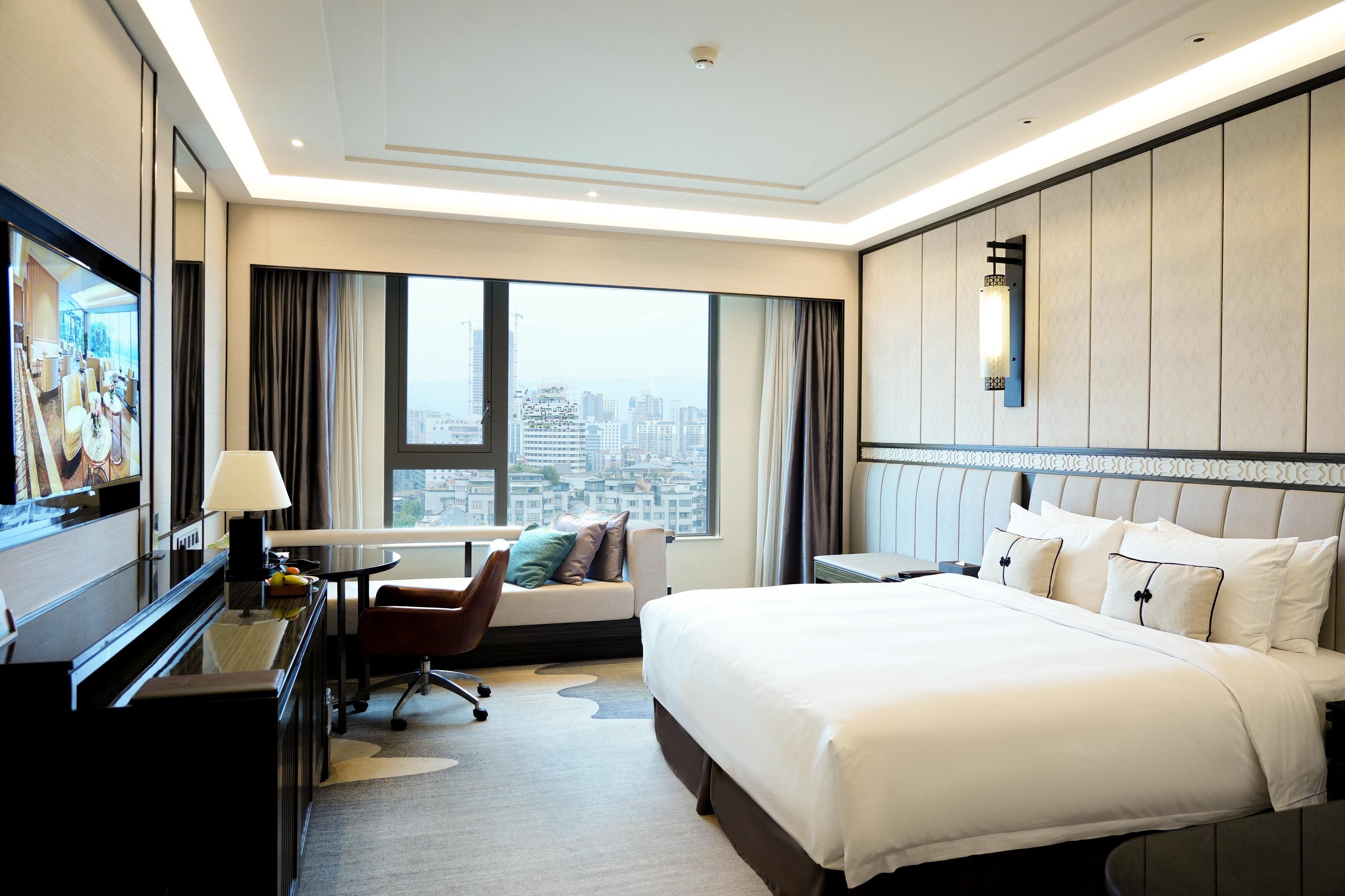 Une chambre d’hôtel avec un lit, un bureau, une chaise, une télévision et une vue sur la ville.