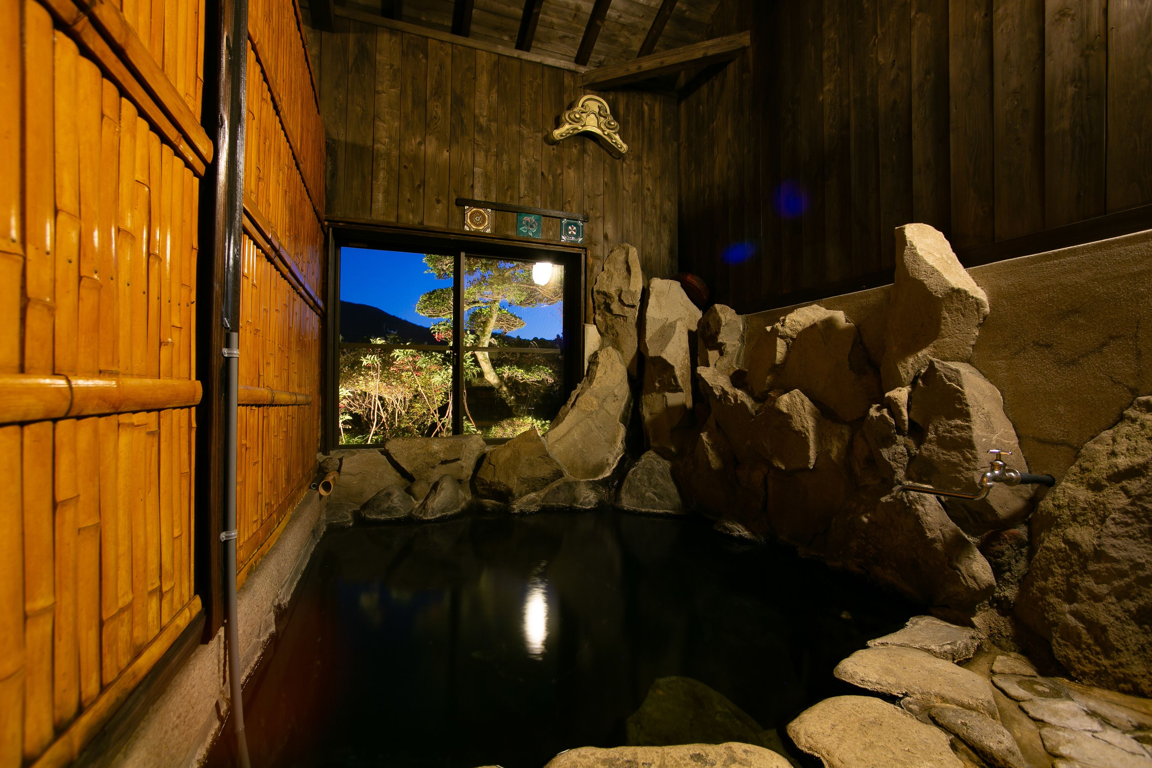 A traditional Japanese onsen with a wooden interior, a stone bath, and a view of a mountain landscape through a window.