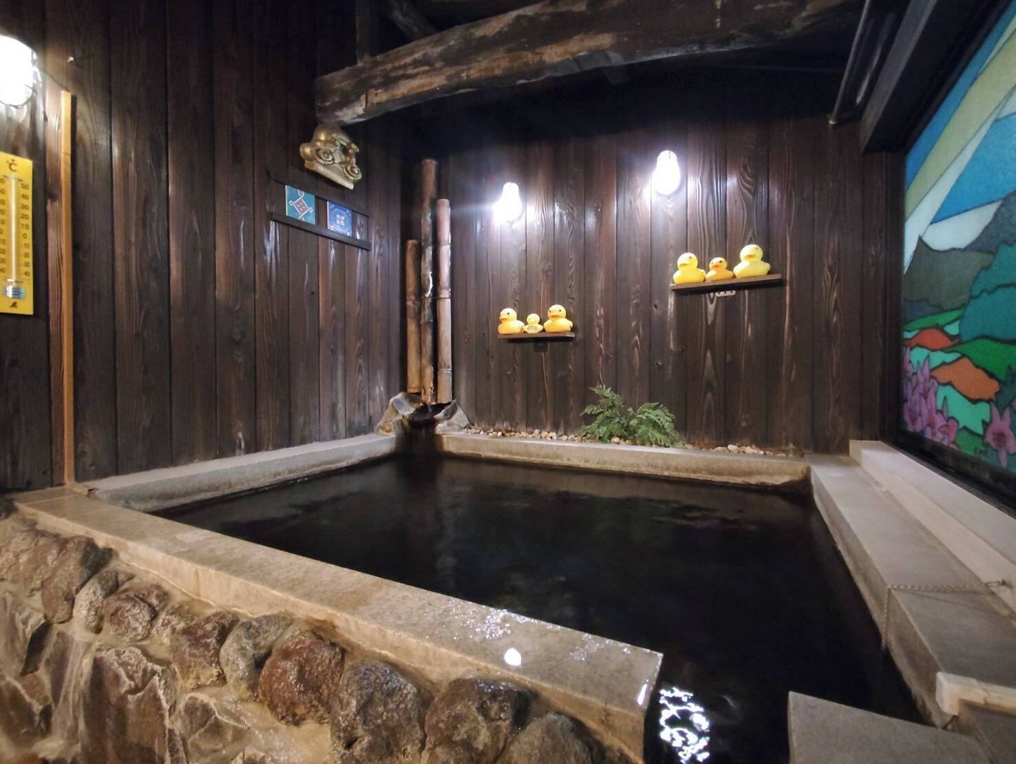 A wooden interior with a stone-lined hot spring, wooden beams, and a mural.