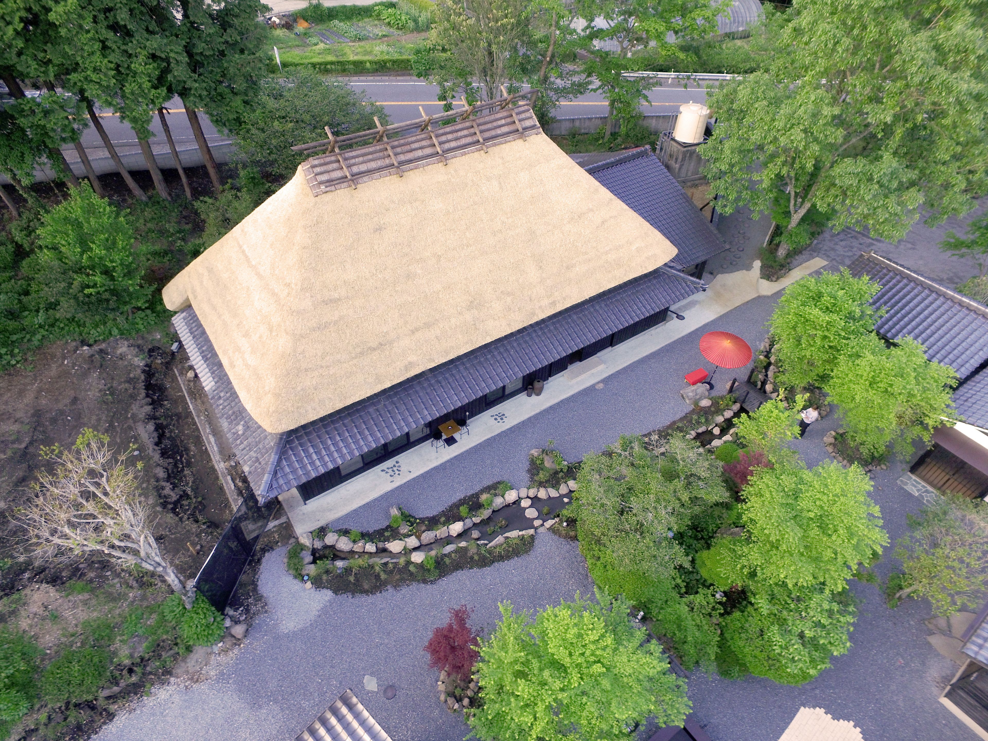 Vista aérea de una edificación tradicional japonesa con techo de paja, un jardín con estanque de carpas y un sendero de piedra.