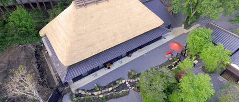 Vista aérea de una edificación tradicional japonesa con techo de paja, un jardín con estanque de carpas y un sendero de piedra.