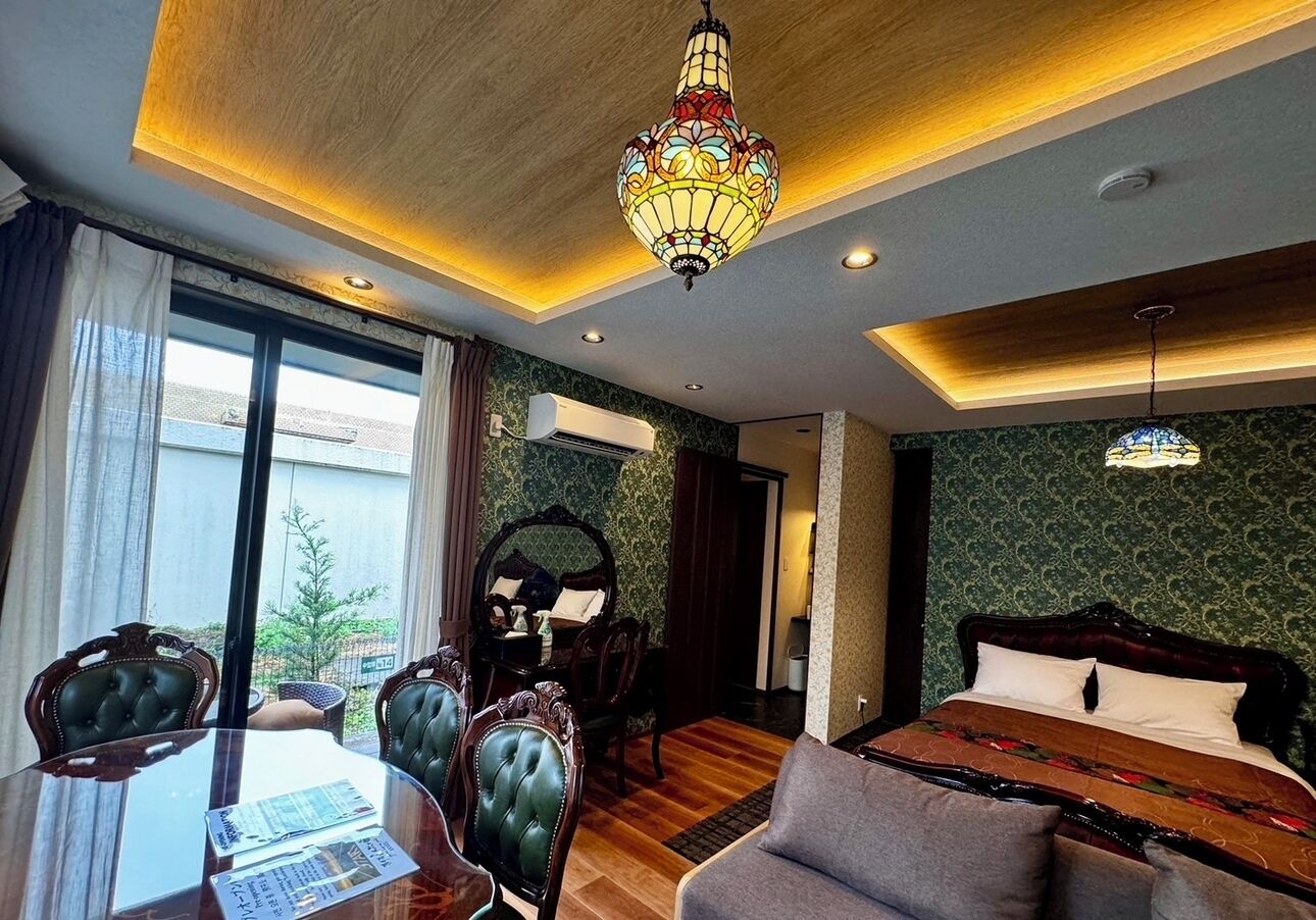 A hotel room with a bed, a dining table with chairs, a chandelier, and a view of the outdoors.