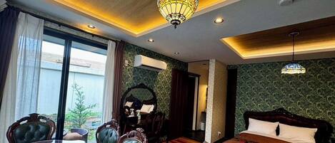 A hotel room with a bed, a dining table with chairs, a chandelier, and a view of the outdoors.