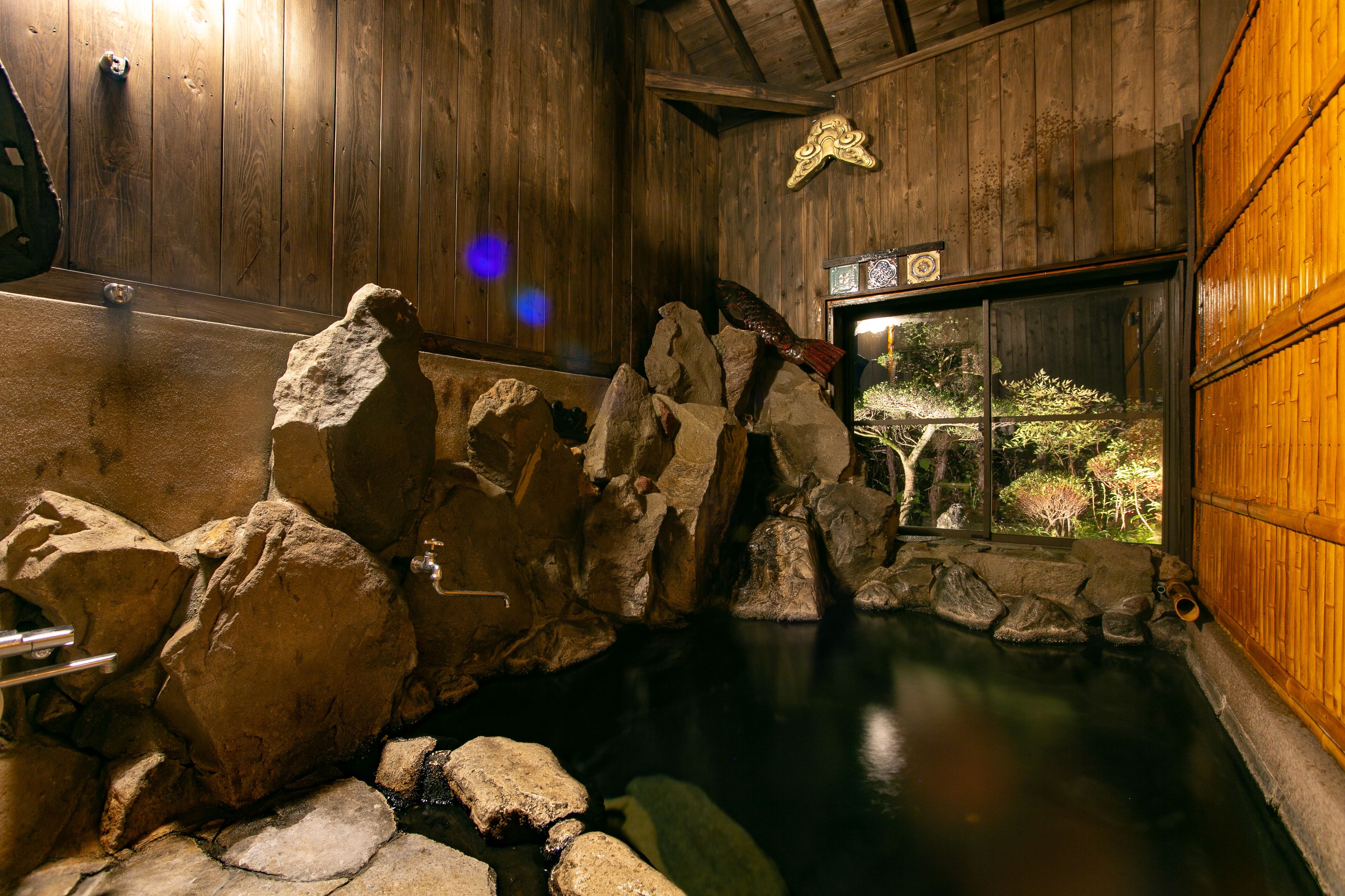 Un bain traditionnel dans une source d’eau chaude, avec des murs en bois et une vue sur la verdure environnante.