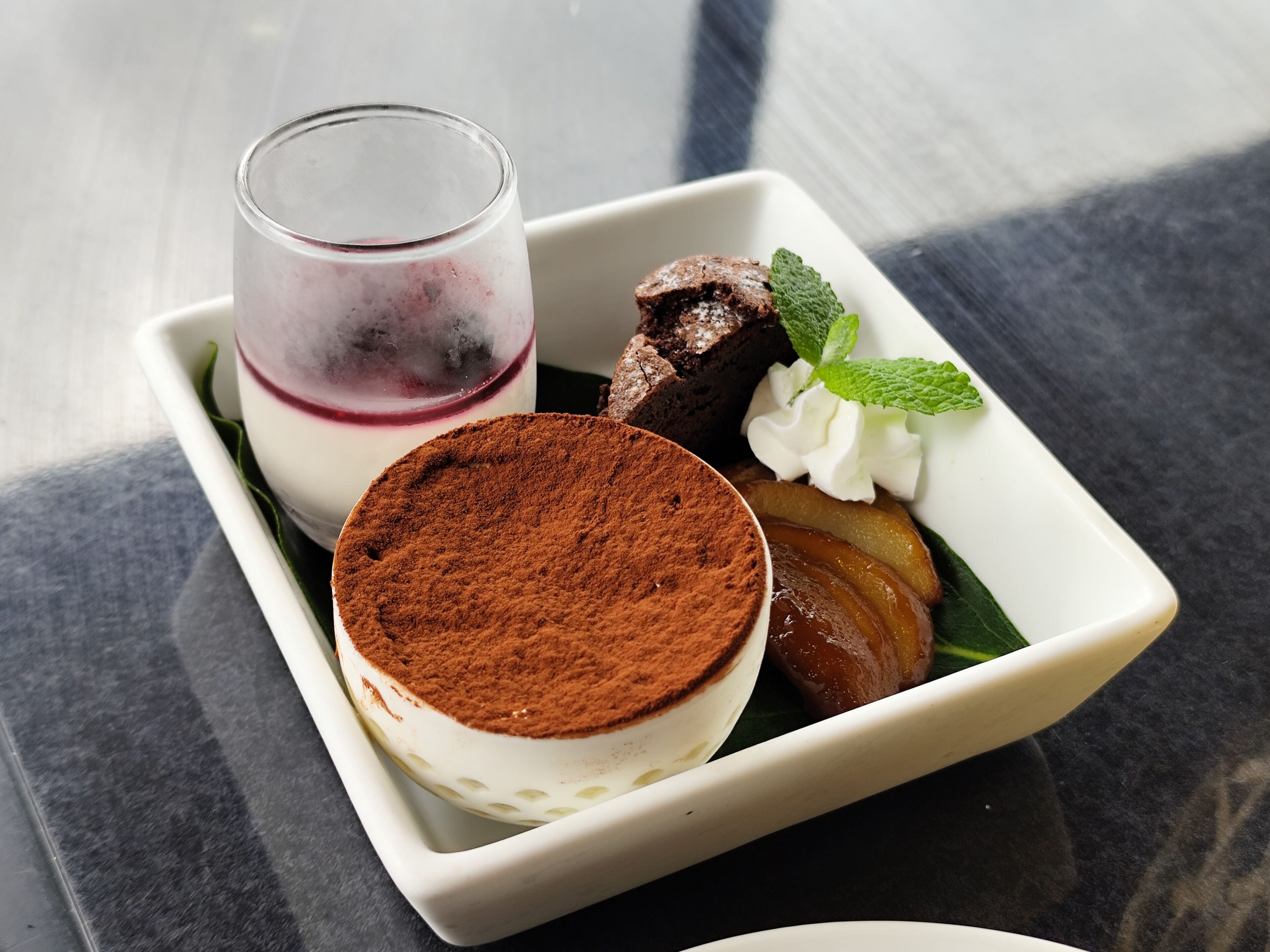 A dessert plate with tiramisu, a scoop of ice cream, a brownie, and a mint garnish.