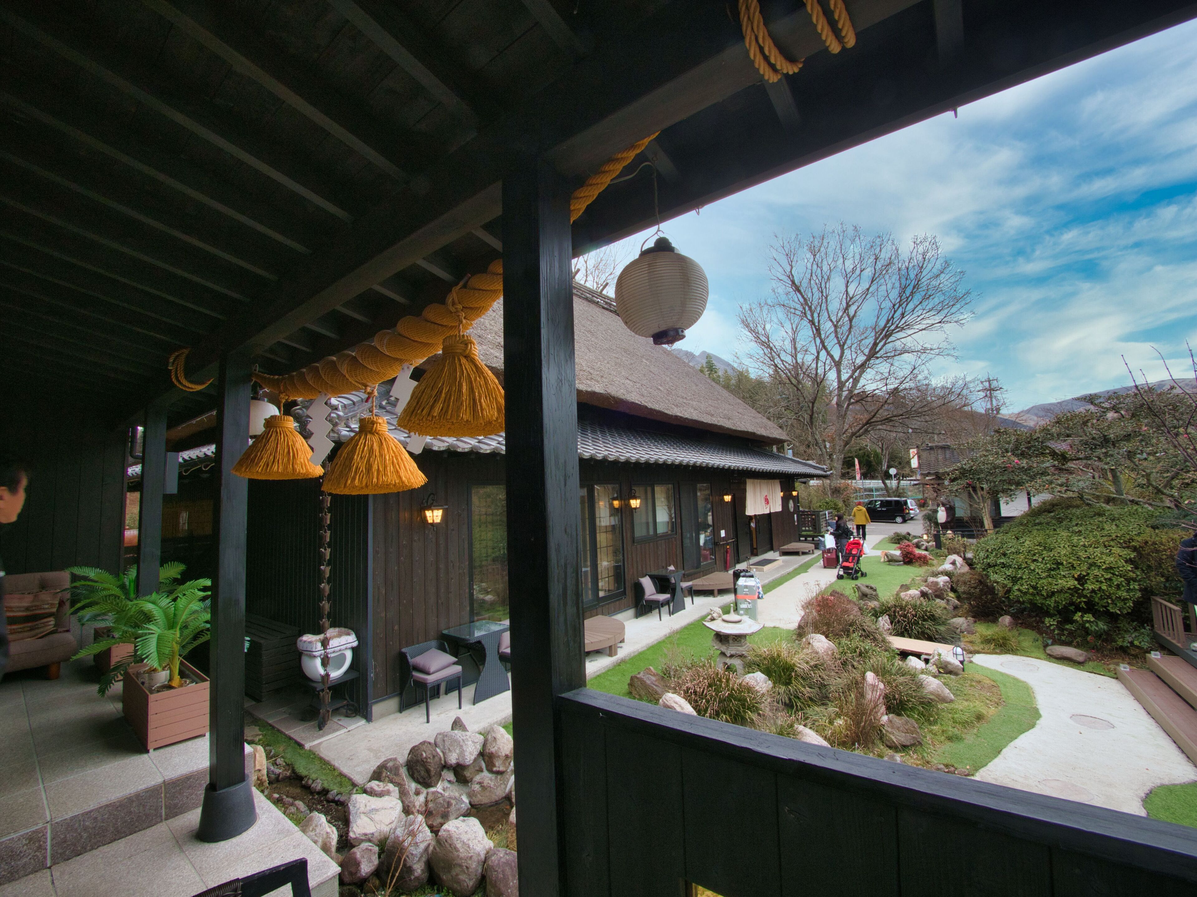 A covered outdoor seating area with wooden tables and chairs, a stone pathway, and a garden with rocks and plants.