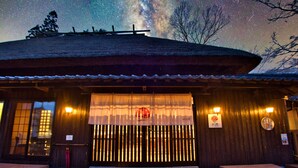 Un edificio japonés tradicional con fachada de madera, tejado de tejas y un cielo nocturno estrellado visible a través de su abertura.