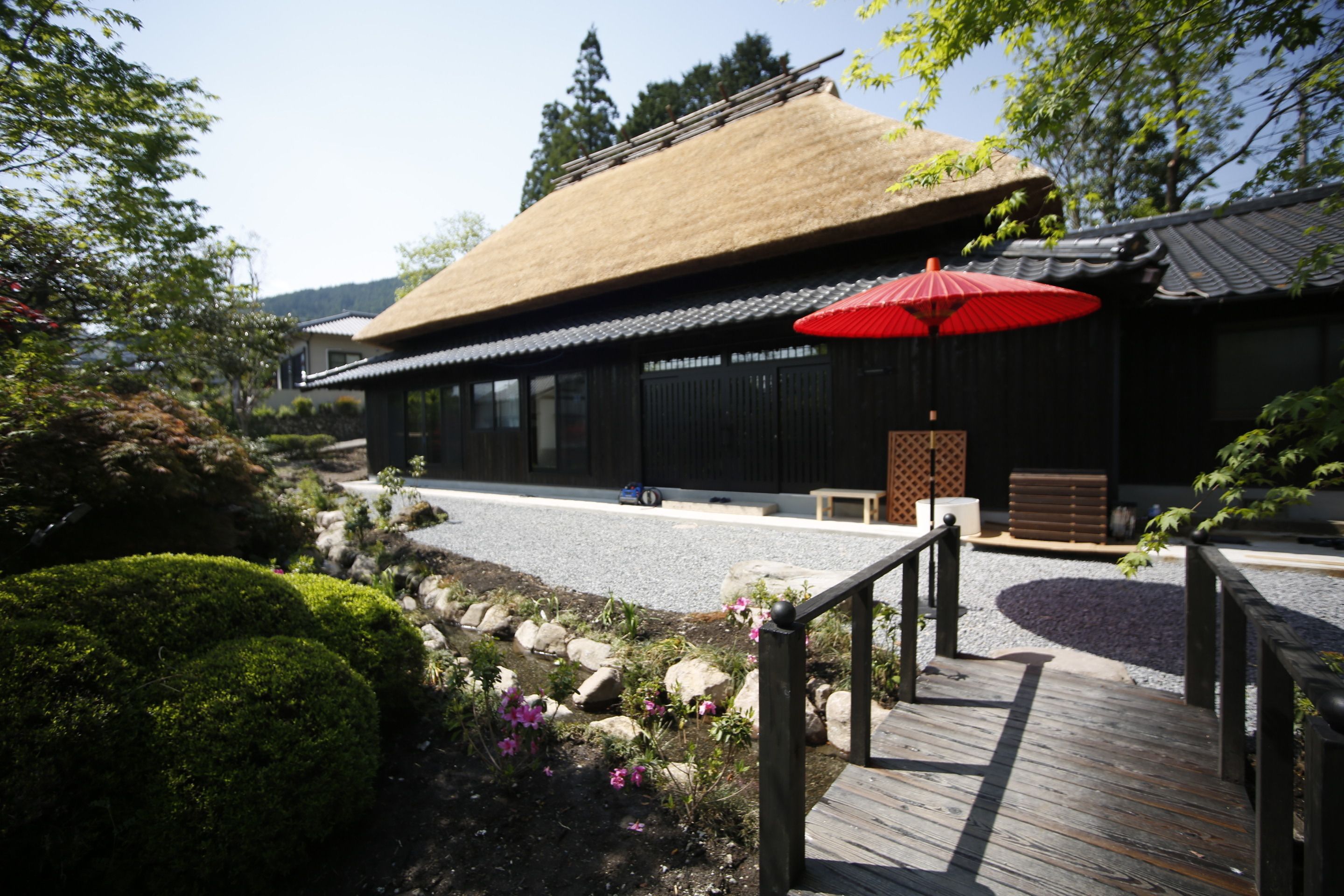 A traditional building with a thatched roof, a wooden deck, and a red umbrella.