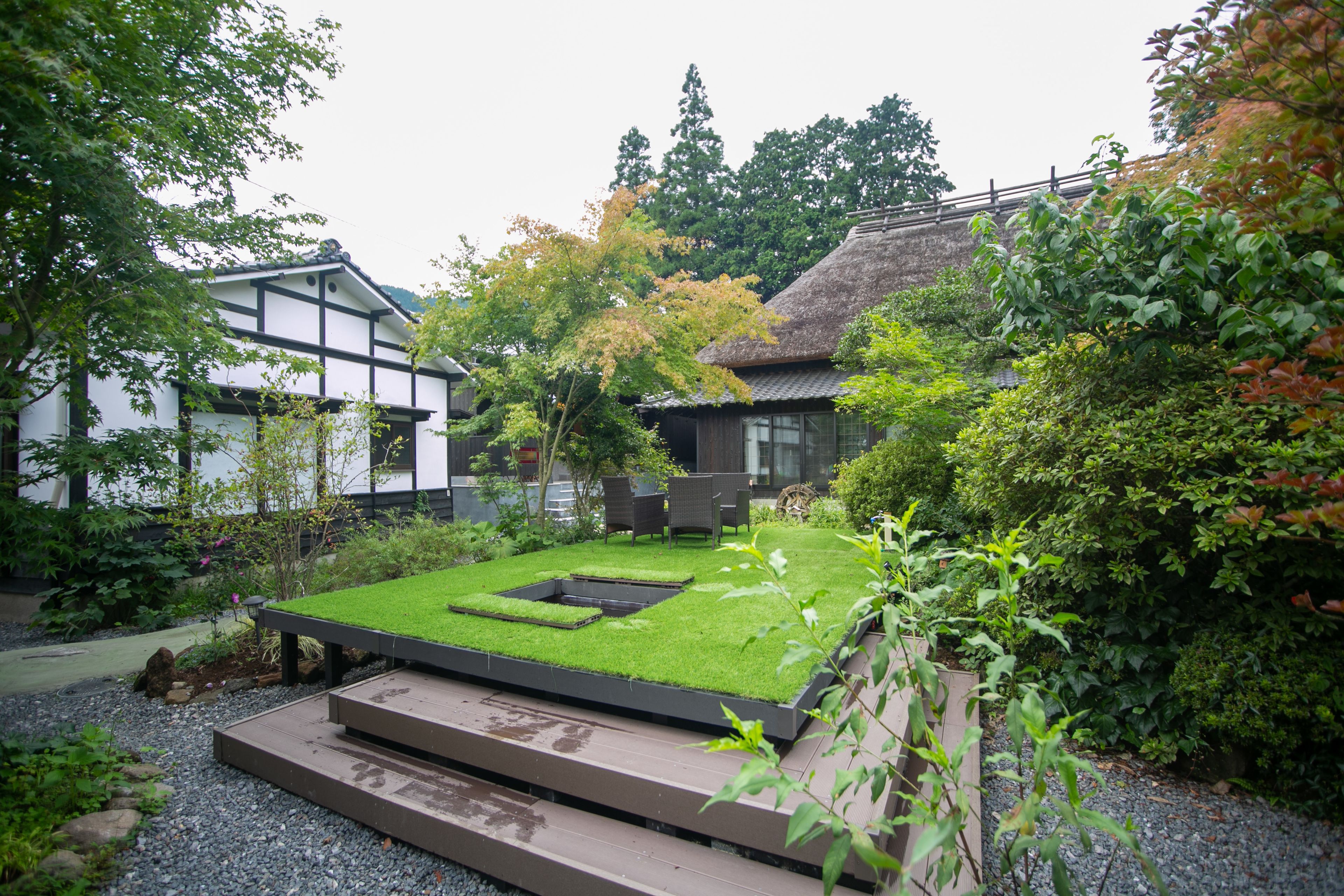 Ein traditioneller japanischer Garten mit einem Gebäude mit Strohdach, einem Teich mit Karpfen und einer hölzernen Terrasse.