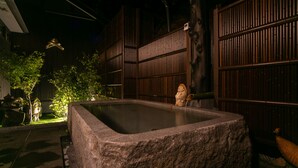 Una bañera de piedra en una habitación tenuemente iluminada, con paredes de madera y una pequeña estatua.